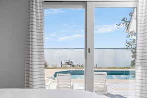 A view from a room with a sliding glass door to a pool area, featuring a clear view of a lake and a dock with a boat. - Deltaville Riverfront Getaway | Discounted rates (Deltaville)