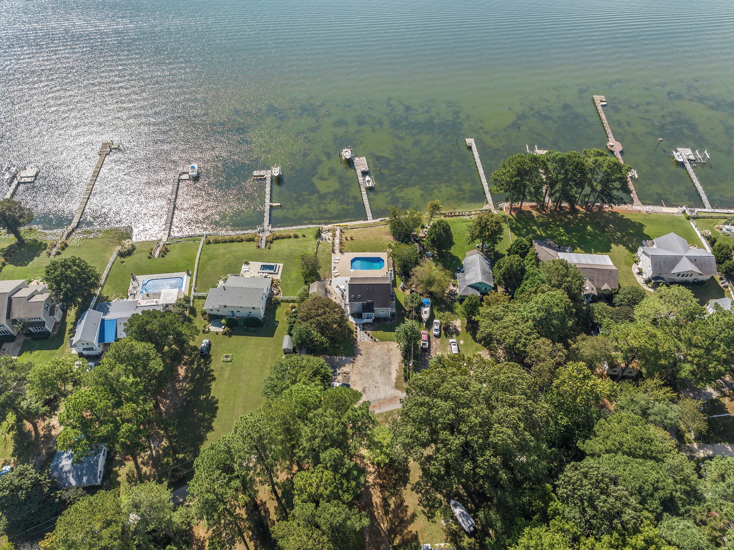 Vue aérienne d’un quartier résidentiel avec des maisons, une piscine et des quais s’étendant dans un lac.