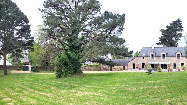 Un bâtiment en pierre doté d’un toit en pente, entouré d’une pelouse bien entretenue et de grands arbres.