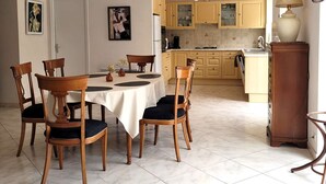 Un coin repas avec une table ronde, six chaises en bois et une nappe blanche. Deux lampes suspendues sont placées au-dessus de la table.