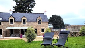 Une maison en pierre dotée d’un patio couvert et de deux chaises de jardin.