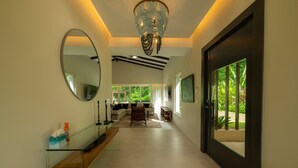 A modern interior with a glass console table, a large mirror, a chandelier, and a view of greenery outside. - Casa Forest 4 bdrs private pool in Los Suenos (Playa Herradura)