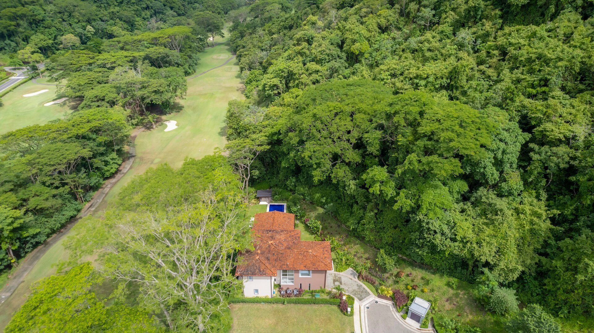 Eine Vogelperspektive zeigt ein Haus, umgeben von dichtem Wald, mit einem sichtbaren Schwimmbad und einem Golfplatz im Hintergrund.