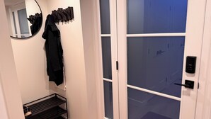 A modern bathroom with a mirror, a black towel rack, a black shelf with a handbag, and a frosted glass door.