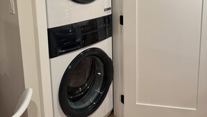 A compact, wall-mounted washer and dryer unit in a room with a wooden floor and a white door.