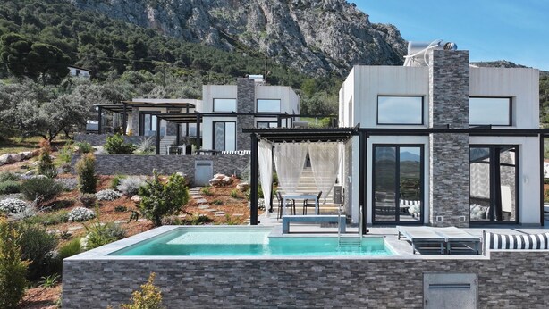 Una villa moderna con piscina, mobiliario exterior y montañas al fondo.