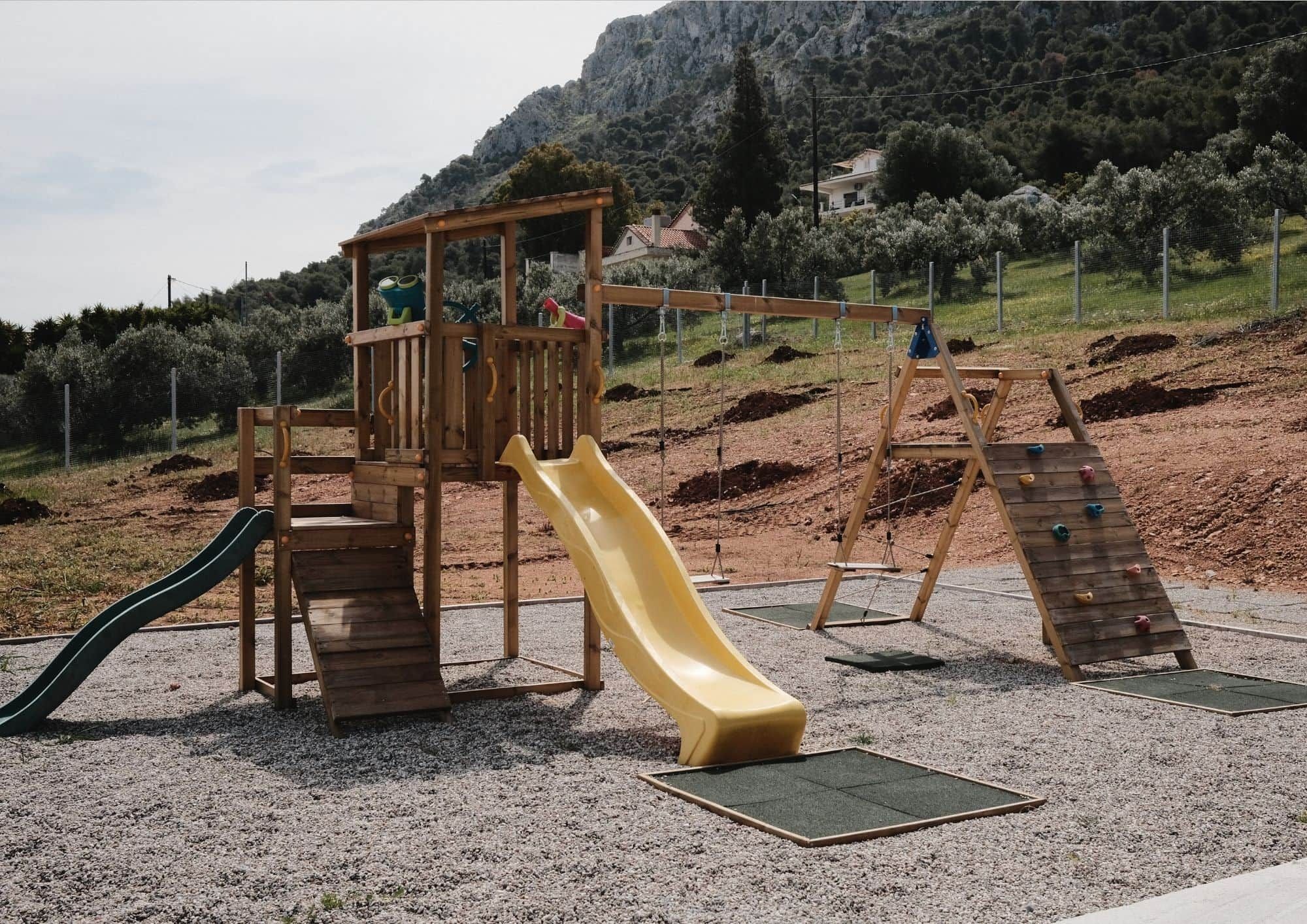 Un parque infantil con un tobogán de madera, pared de escalada y una estructura de madera para trepar.
