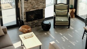 Una sala de estar moderna con una pared de piedra, un televisor de pantalla plana, una chimenea, un sofá, una mesa de centro y lámparas colgantes.