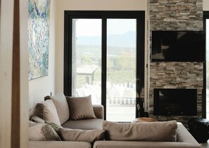 Un salon avec un canapé, un téléviseur à écran plat, un mur en pierre et une grande fenêtre donnant sur un beau paysage.