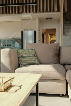 A modern living room with a beige sofa, a patterned throw pillow, and a wooden coffee table. - T H A L I A  -  Aelia Horizon Villas (Corinth)