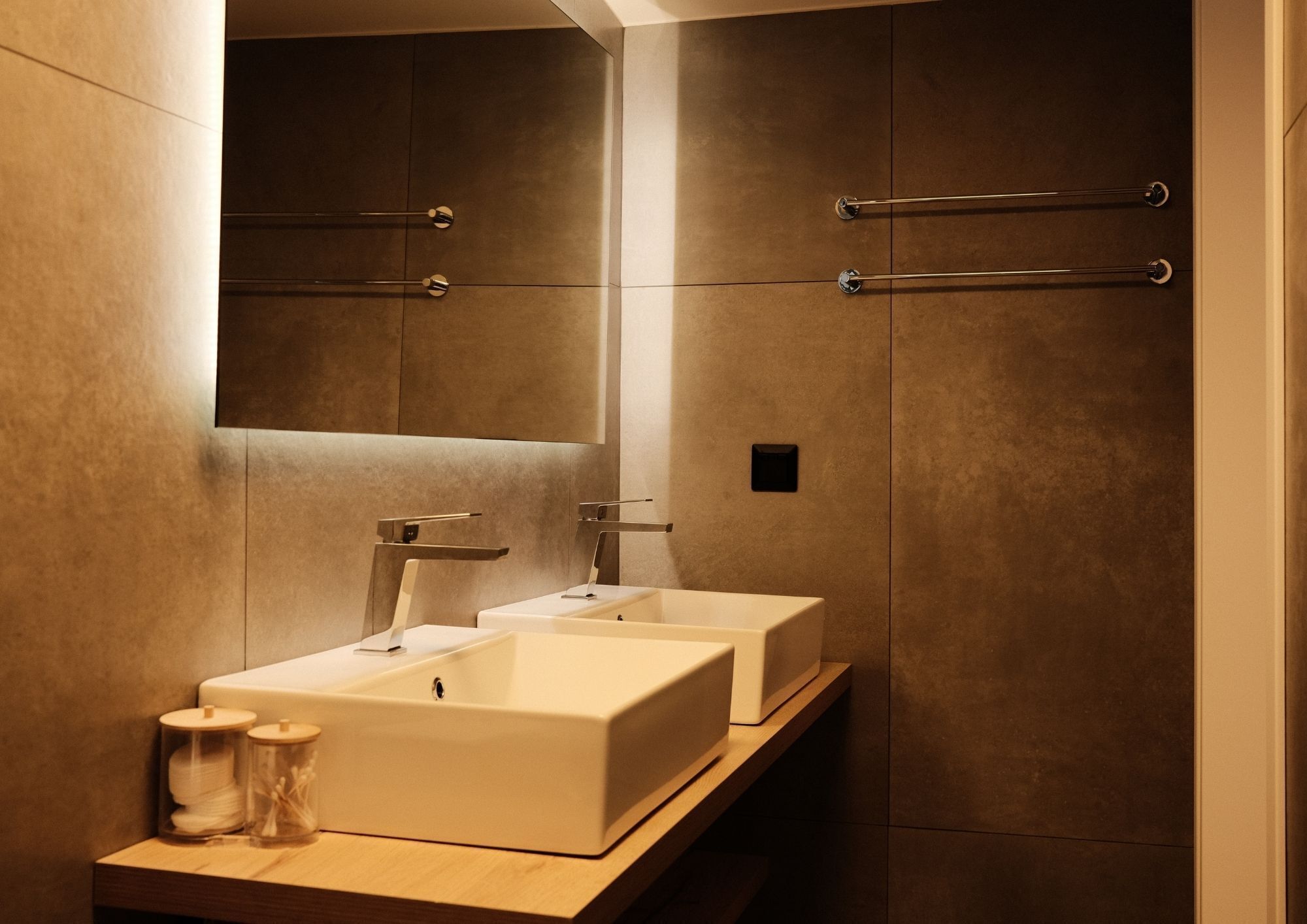 Un baño moderno con dos lavamanos, un espejo y barras para toallas.