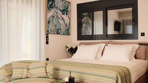 A hotel room with a bed, a chair, a small table, and a painting on the wall.