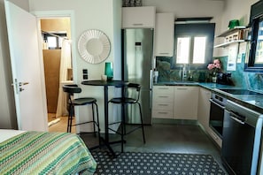 Una cocina compacta equipada con refrigerador, estufa y lavavajillas. Hay un pequeño comedor con taburetes y una mesa.
