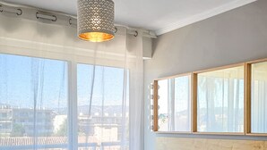 A neatly made bed with white linens and rolled towels, a wooden headboard, and a large window with curtains.