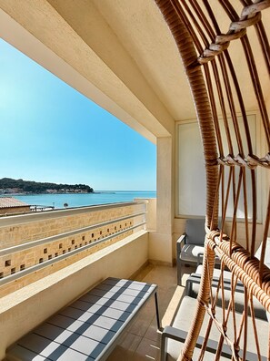 A balcony with a view of the sea, a wicker chair, and a tiled table.