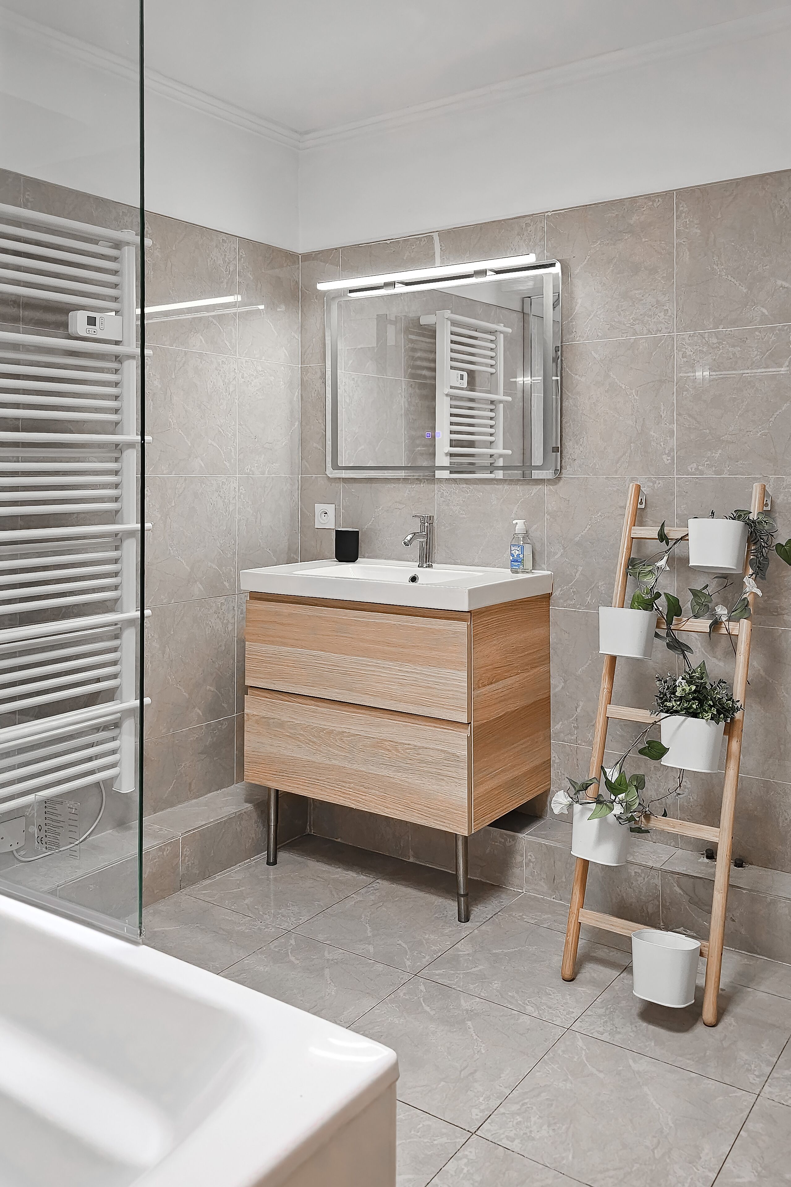 Un baño moderno con cabina de ducha de vidrio, tocador de madera con espejo y estante para plantas.