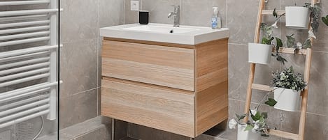Un baño moderno con cabina de ducha de vidrio, tocador de madera con espejo y estante para plantas.