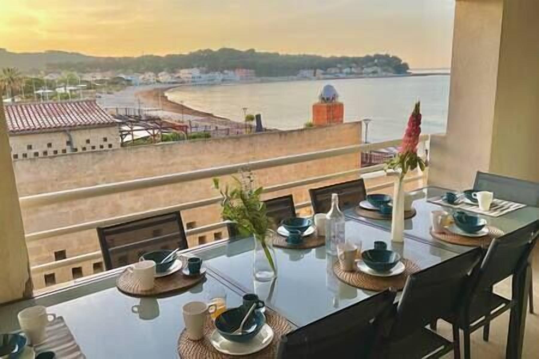 Une table à manger offrant une vue sur une zone côtière, notamment une plage et des bâtiments situés au loin.