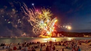 Ein Strand mit Menschen, die am Sand sitzen und in der Ferne Feuerwerk beobachten.