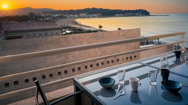 Ein Balkon mit Tisch für zwei Personen, Blick auf Strand und Sonnenuntergang.