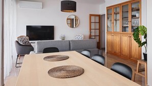 Una sala de estar moderna con televisión de pantalla plana, sofá gris, mesa de comedor de madera y un aparador con puertas de vidrio.