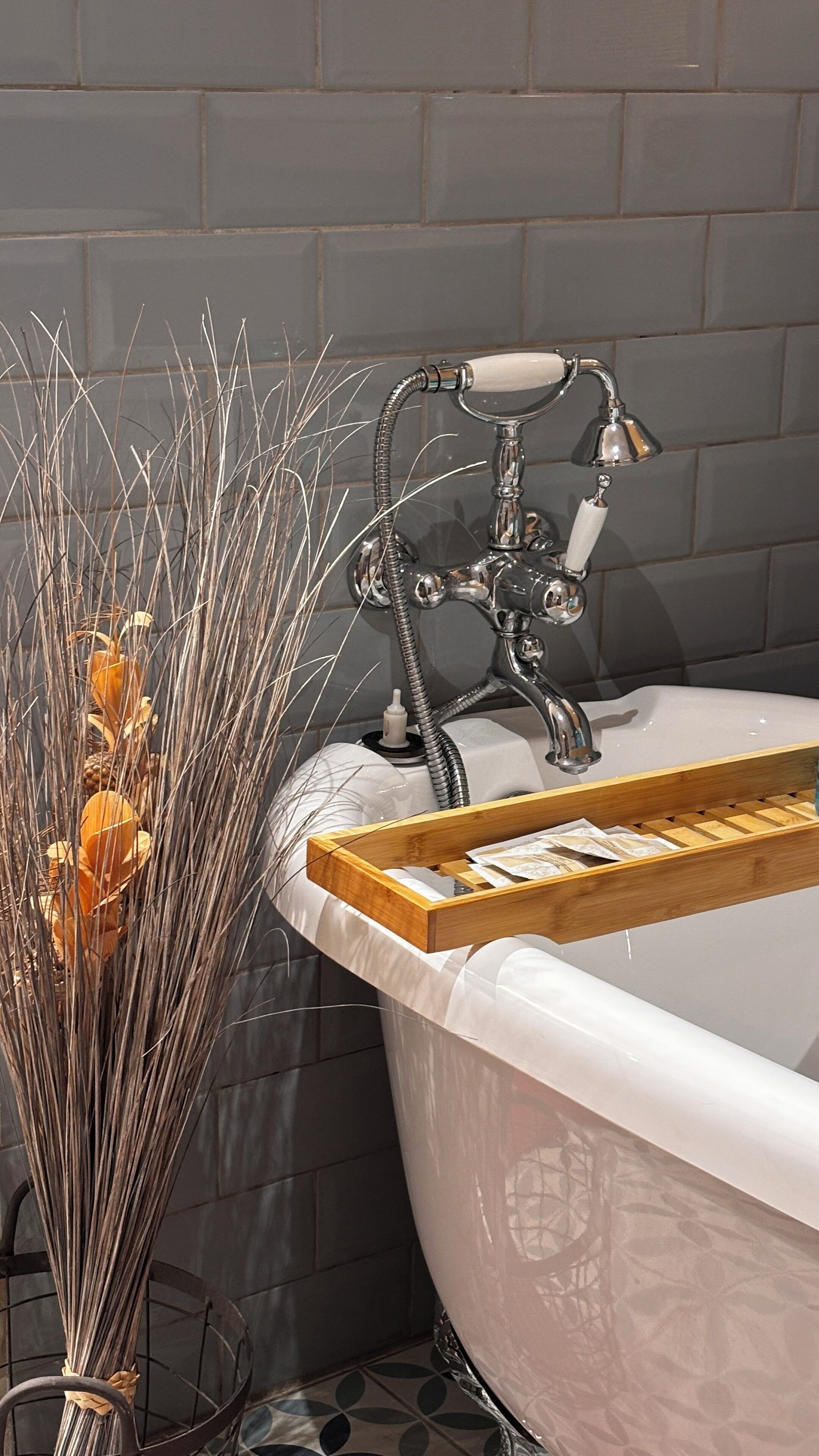 Une baignoire avec un plateau en bois, un robinet en métal et un vase contenant des plantes séchées.