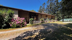 A two-story house with a covered porch, a gravel driveway, and a well-maintained garden with pink flowers.