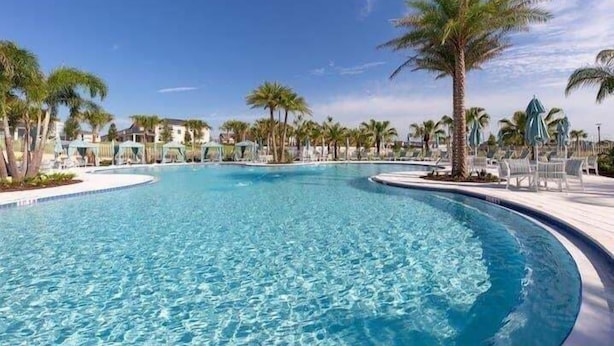 Una piscina con palmeras, sillas de descanso y un cielo despejado.