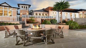 Un patio con mobiliario exterior y una chimenea, rodeado de edificios con balcones y un muro de piedra.