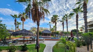Un espace aménagé au bord de la piscine, avec des chaises longues, une piscine et des palmiers.
