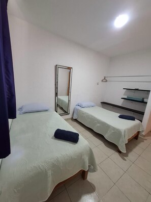 Ein Zimmer mit zwei Betten, einem Spiegel, einem Regal und einer Kleiderstange.