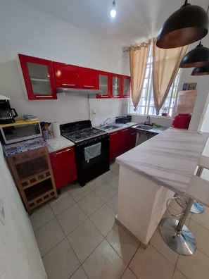 Una cucina compatta con mobili rossi, un fornello a gas, un lavello e un piccolo ripiano.