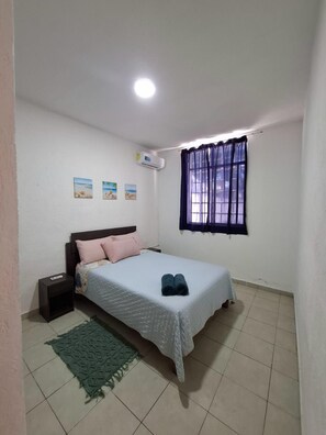 A bedroom with a bed, a nightstand, a wall-mounted air conditioner, a window with curtains, and three small wall art pieces.