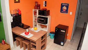Uma cozinha compacta com mesa de madeira, micro-ondas, cafeteira e geladeira.