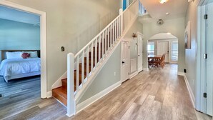 A spacious hallway with a wooden staircase, a dining area with a table and chairs, and a bedroom with a bed and a nightstand. - HUGE % OFF, Private Pool ☀️ Walk to Beach, Screened Porch, 6 Bdrm ☀️ Big Driveway (Seagrove Beach)