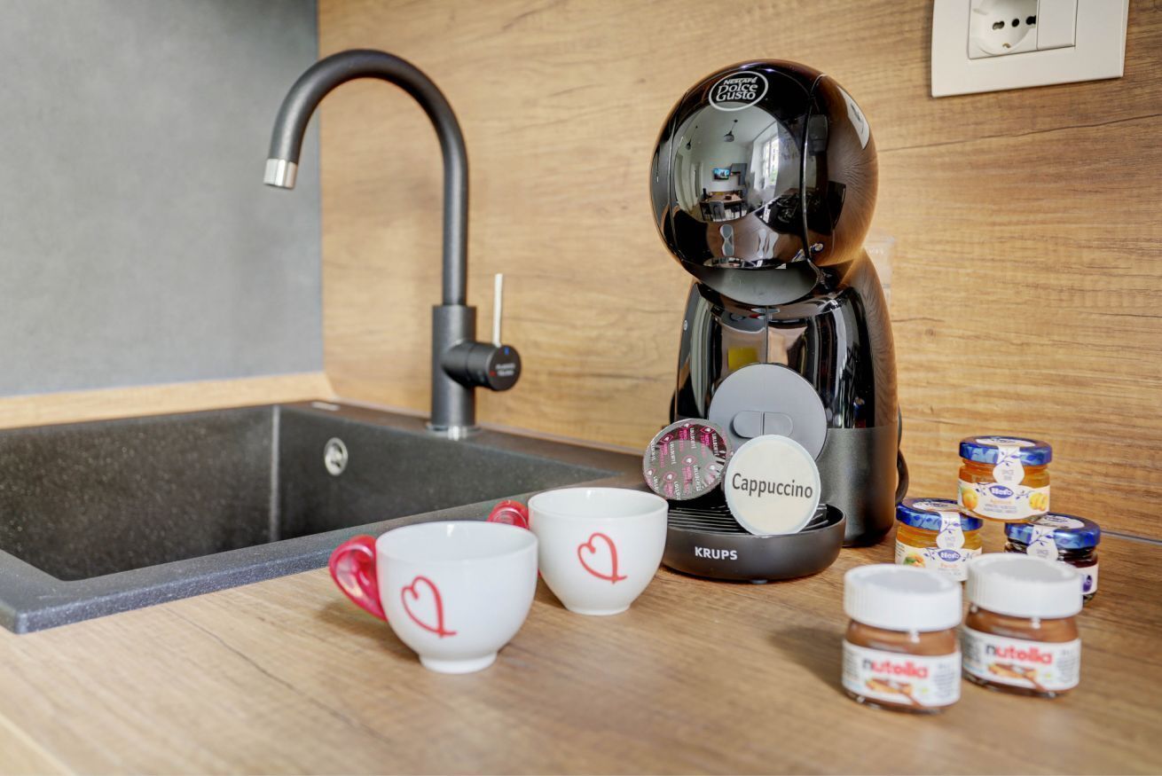 Ett kök med en kaffebryggare, två koppar och burkar med Nutella och andra pålägg.
