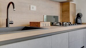 A modern kitchen with a wooden backsplash, a built-in sink, a coffee machine, and a tea box. - SAN GIOVANNI COZY APT - HOME AND MORE (Roma)