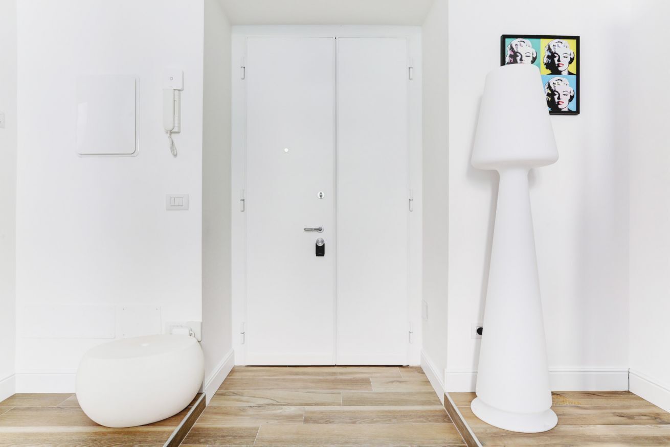 A white door with a keyhole and a handle, a white floor lamp, and a white toilet.