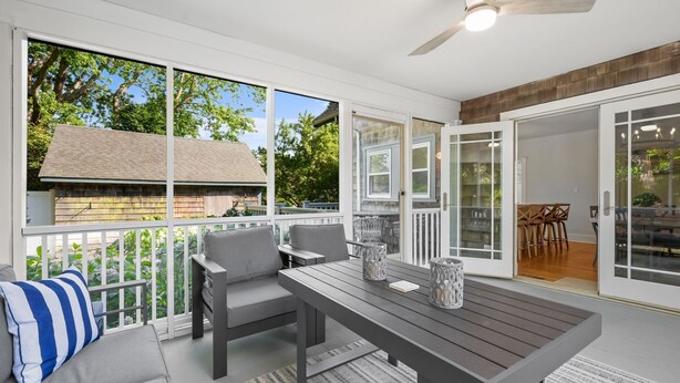 A covered patio with a table and chairs, a ceiling fan, and a view of a house through large windows. - Your Cape State of Mind Adventure Awaits! (South Yarmouth)