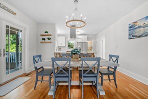 A modern dining area with a central table, blue chairs, and a chandelier. - Your Cape State of Mind Adventure Awaits! (South Yarmouth)