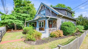 A two-story house with a porch, surrounded by a wooden fence and various trees. - Your Cape State of Mind Adventure Awaits! (South Yarmouth)