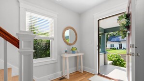 A clean, modern entryway with a wooden staircase, a white console table with a mirror, and a view of a house through a glass door. - Your Cape State of Mind Adventure Awaits! (South Yarmouth)