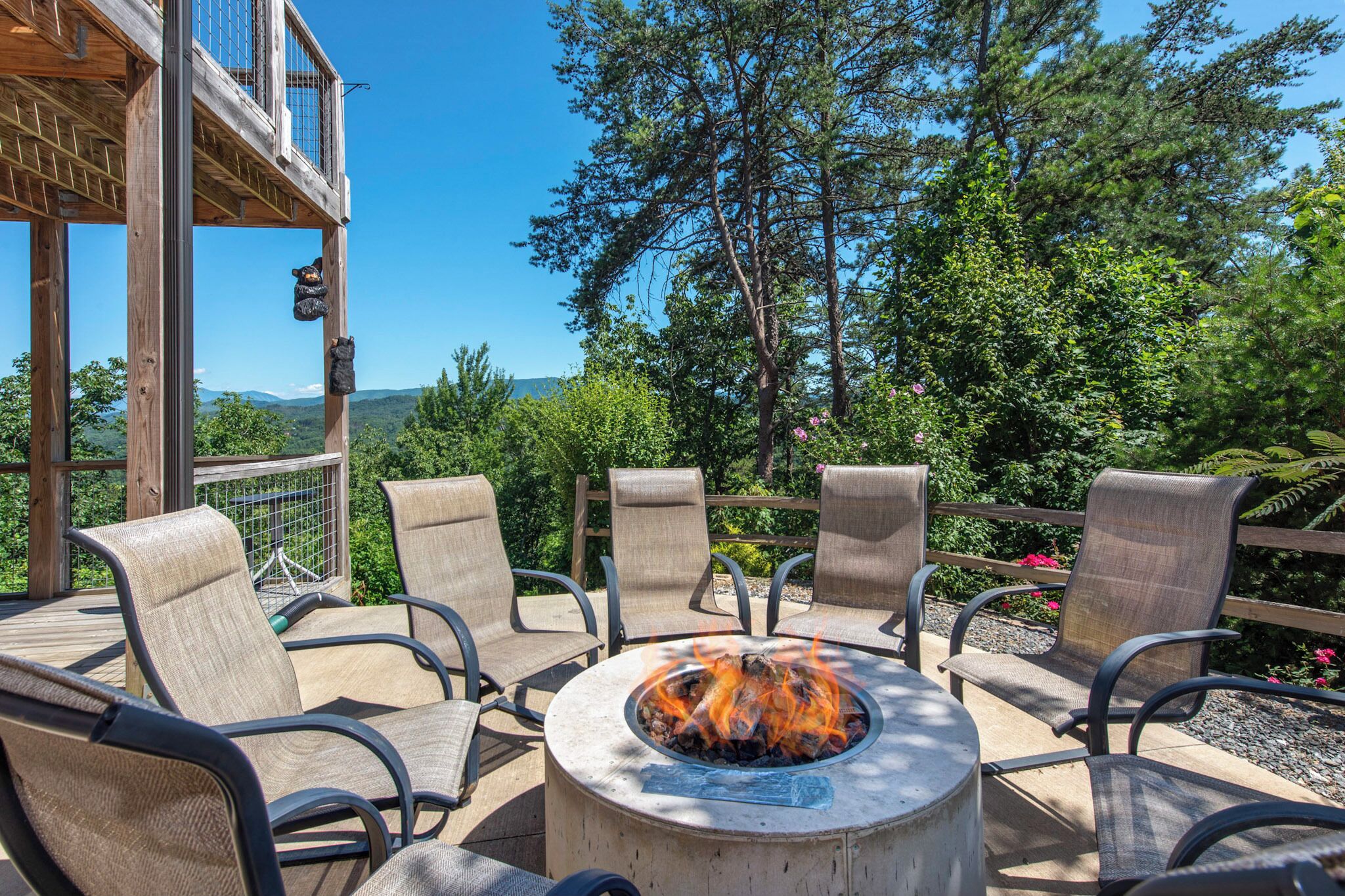 A fire pit surrounded by chairs on an outdoor deck with a view of trees and hills.