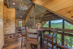 A wooden cabin interior with a dining area, a ceiling fan, and a view of the forest. - Barefoot Landing (Sevierville)