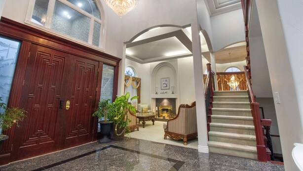 A grand foyer with a wooden double door, a chandelier, a fireplace, and a staircase. - Panridge Estate (Surrey)