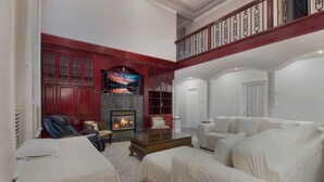 A spacious living room with a fireplace, a television, and a high ceiling with decorative railings. - Panridge Estate (Surrey)