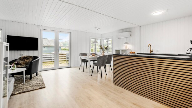 Une cuisine moderne avec un plan de travail en bois, un coin repas avec une table et des chaises, et un téléviseur fixé au mur.