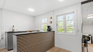 Une cuisine moderne avec un îlot central aux panneaux de bois, des murs blancs et de grandes fenêtres.