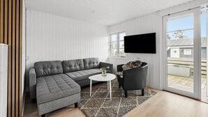 Un salon moderne avec un canapé gris, un fauteuil noir, une petite table ronde et un téléviseur à écran plat fixé au mur.