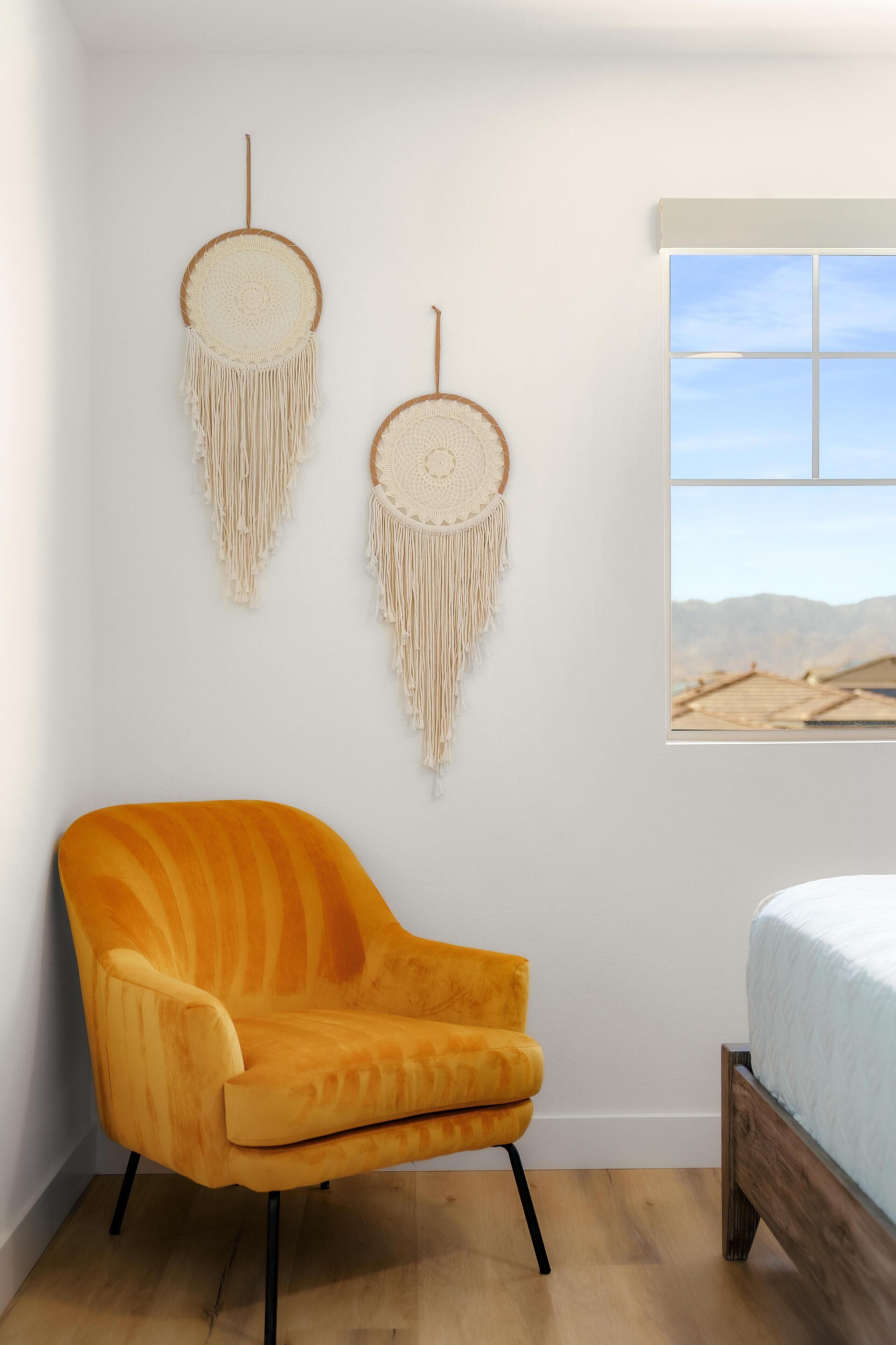 A bedroom with a wooden bed, a yellow armchair, and two macramé wall hangings.